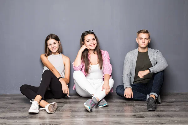 Gruppe von Freunden sitzt auf dem Boden vor grauem Hintergrund — Stockfoto