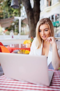 Dizüstü bilgisayarda çalışan ve kafe mekanlarda otururken gülümseyen güzel genç kadın