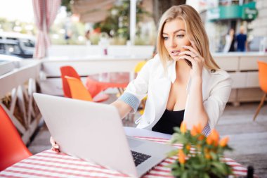 Genç güzel kadın akıllı telefon konuşmayı önünde otururken cafe bar, çekici erkek kadın kahvaltı kahve dükkanında onu hücre telefon ile çağıran dizüstü bilgisayar açık