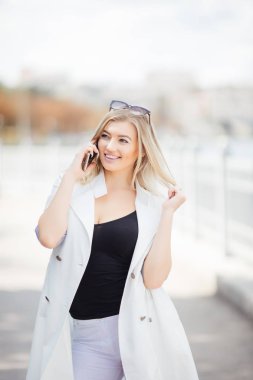 Genç kadın konuşma, açık havada granit set karşı bir nehir üzerinde o duruyor dinlerken cep telefonu üzerinde söz