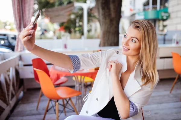 Gyönyörű fiatal nőt is csinál használ egy okos telefon, és mosolyogva, miközben pihen a kávézó selfie — Stock Fotó