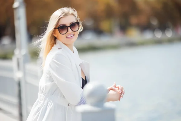 Vacker ung kvinna poserar som modell står på vallen nära havet eller ocean. Lady bär casual och solglasögon. — Stockfoto