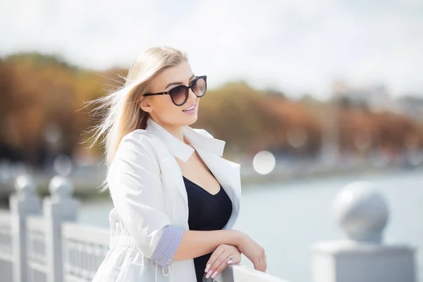 Hermosa mujer joven haciéndose pasar por modelo de pie en el terraplén cerca del mar o el océano. Señora vistiendo gafas de sol y casual . — Foto de Stock