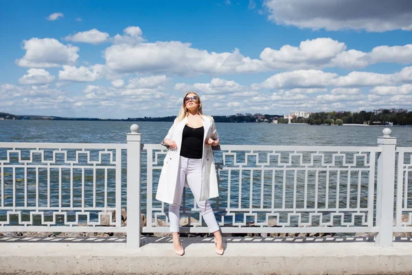 Ganska ung blond kvinna står vid vallen havsstranden i den nedgående solen strålar — Stockfoto