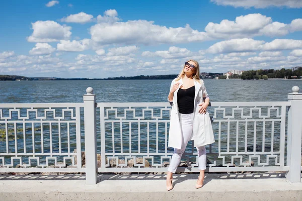 Ganska ung blond kvinna står vid vallen havsstranden i den nedgående solen strålar — Stockfoto