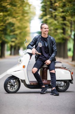 Neşeli genç adam şehirde scooter üzerinde biniyor.