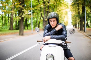 Yakışıklı adam kameraya bakıyor ve onun scooter üzerinde otururken gülümseyen