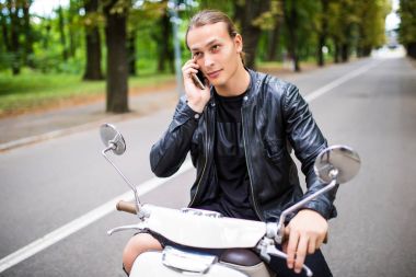 Scooter üzerinde oturan ve cep telefonda konuşurken neşeli genç adam