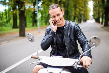 Scooter üzerinde oturan ve akıllı telefon kullanarak adam genç gülümsemek