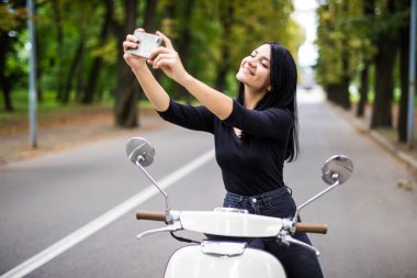 Bir vintage scooter ve yapmak bir selfie telefon şehirde oturan genç kadın
