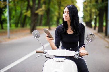 Gülümseyen genç kadın cep telefonu, scooter üzerinde oturan bakarak