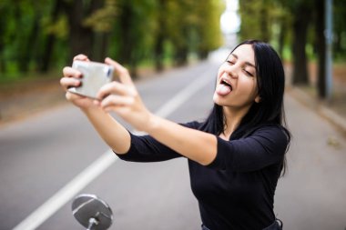 Açık selfie akıllı telefonunu alarak scooter üzerinde oturan genç ve güzel kadın portresi.