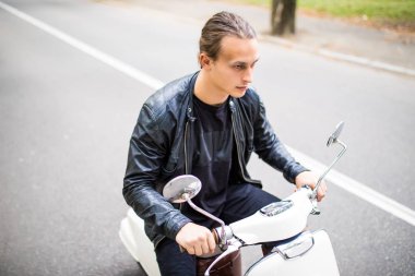 Kask içinde neşeli genç adam scooter şehirdeki sokak üzerinde biniyor.