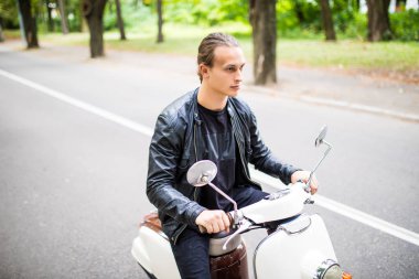 Kask içinde neşeli genç adam scooter şehirdeki sokak üzerinde biniyor.