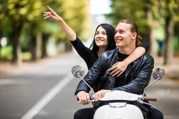 Glamourosa jovem casal montando scooter na rua, Mulher apontou para o lado, homem olhar da mesma maneira — Fotografia de Stock