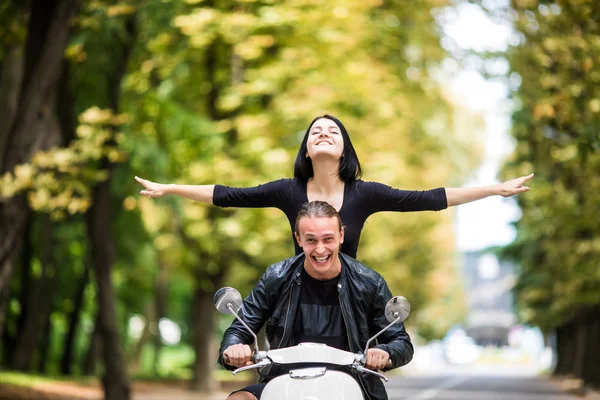Güzel genç çift sürme scooter mutlu kadın uzanmış silah tutmak birlikte ve gülümseyen