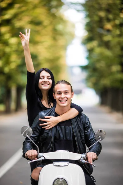 A cavalgar com diversão. Belo jovem casal montando scooter juntos, enquanto a mulher feliz levantando braços e sorrindo. Passeio e amor — Fotografia de Stock