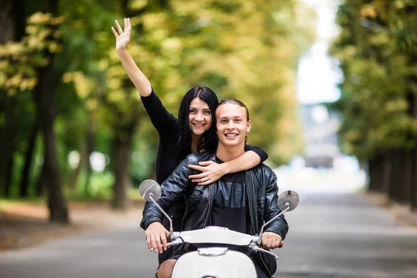 Ездить с удовольствием. Красивая молодая пара едет скутер вместе в то время как счастливая женщина поднимает руки и улыбается. Поездка и любовь — стоковое фото