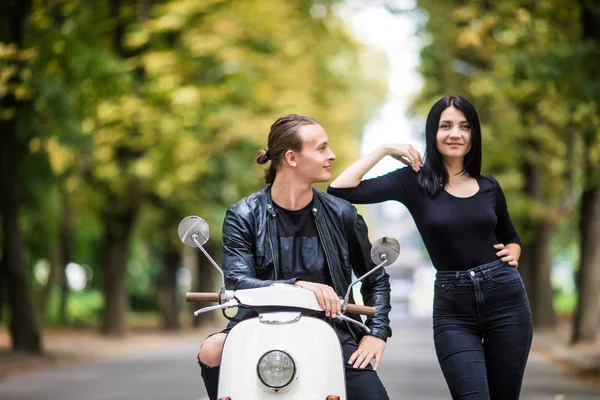 Beautiful young couple talking and smiling while sitting on scooter outdoors — Stock Photo, Image