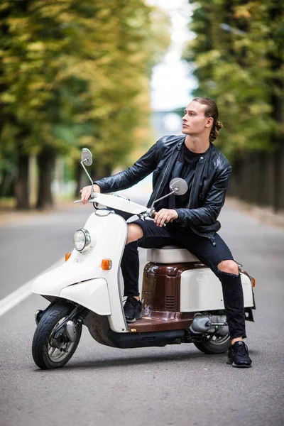 Neşeli genç adam şehirde scooter üzerinde biniyor.