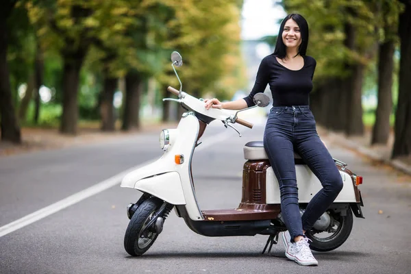 Kasabanın dar sokakta moto scooter üzerinde oturan rahat genç kadın.