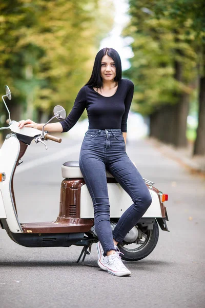Jovem mulher casual sentado em moto scooter na rua estreita na cidade . — Fotografia de Stock
