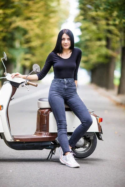 Kasabanın dar sokakta moto scooter üzerinde oturan rahat genç kadın.