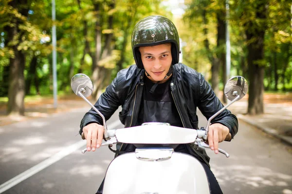 Kask içinde neşeli genç adam şehirde scooter üzerinde biniyor.