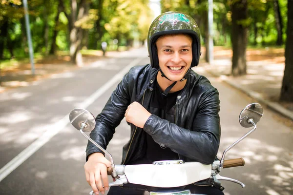 Bonito homem está olhando para a câmera e sorrindo enquanto sentado em sua scooter — Fotografia de Stock