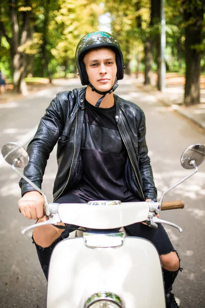 Hombre guapo está mirando a la cámara y sonriendo mientras está sentado en su scooter — Foto de Stock