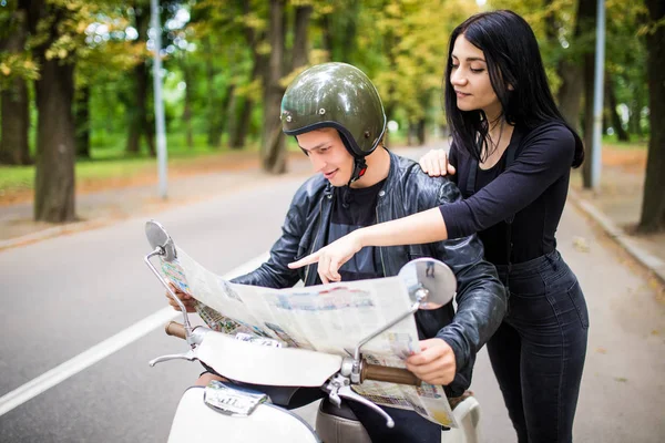 Mooie jonge verliefde paar zittend op scooter samen en onderzoekt kaart terwijl vrouw wijzen het en glimlachen — Stockfoto