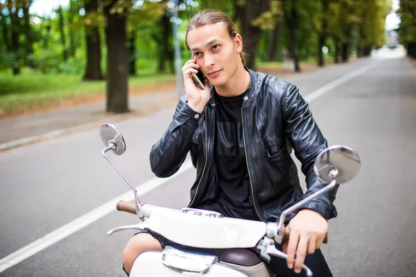 Scooter üzerinde oturan ve cep telefonda konuşurken neşeli genç adam