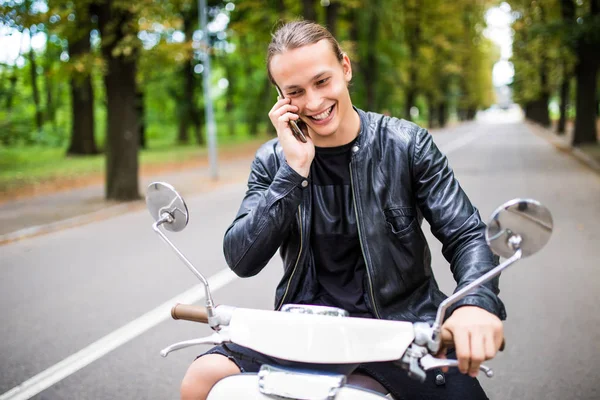 Scooter üzerinde oturan ve akıllı telefon kullanarak adam genç gülümsemek