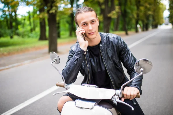 Scooter üzerinde oturan ve akıllı telefon kullanarak adam genç gülümsemek