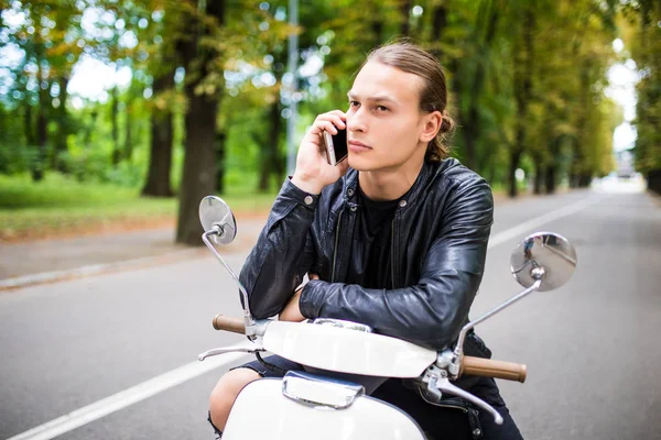 Jovem homem bonito sentado em scooter e usando telefone inteligente — Fotografia de Stock