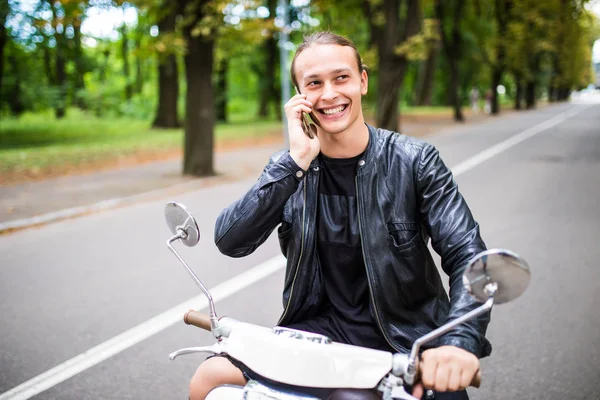 Jovem alegre sentado em scooter e falando no telefone celular — Fotografia de Stock