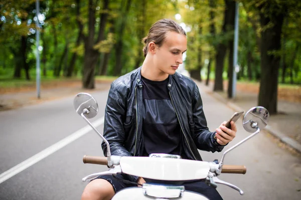 Jovem homem bonito sentado em scooter e usando telefone inteligente — Fotografia de Stock