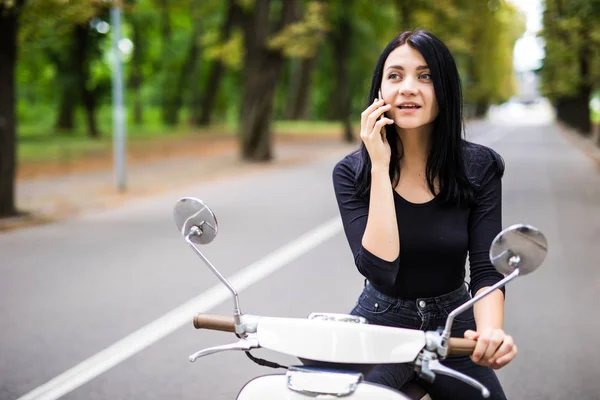 Mulher bonita vestida casual sentado em scooter e falando por telefone . — Fotografia de Stock