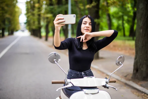 Bir vintage scooter ve yapmak bir selfie telefon şehirde oturan genç kadın