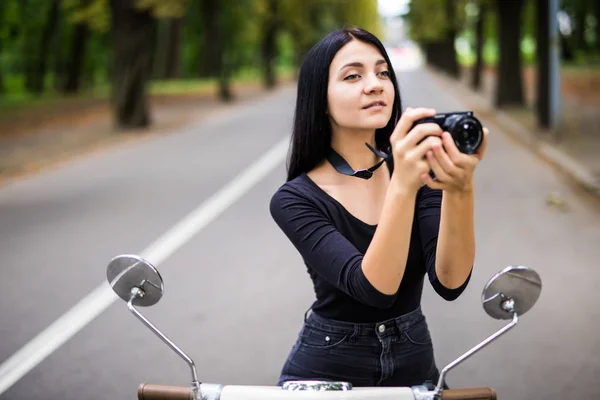 Jovem bela mulher hipster montando com câmera de foto na rua da cidade de moto, tirando fotos . — Fotografia de Stock