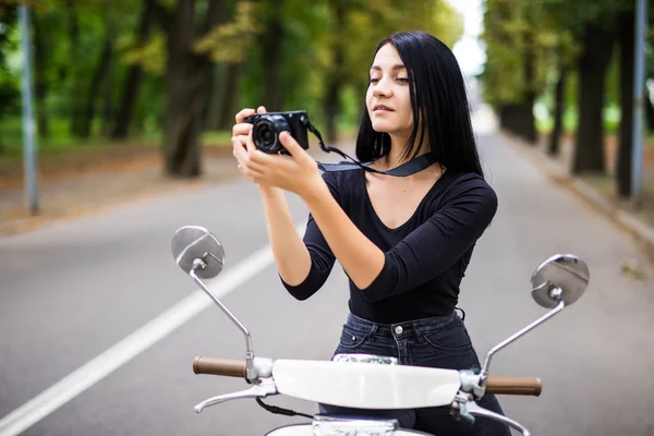 young beautiful hipster woman riding with photo camera on motorbike city street, taking pictures.