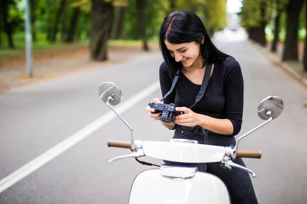 Jovem bela mulher hipster montando com câmera de foto na rua da cidade de moto, tirando fotos . — Fotografia de Stock