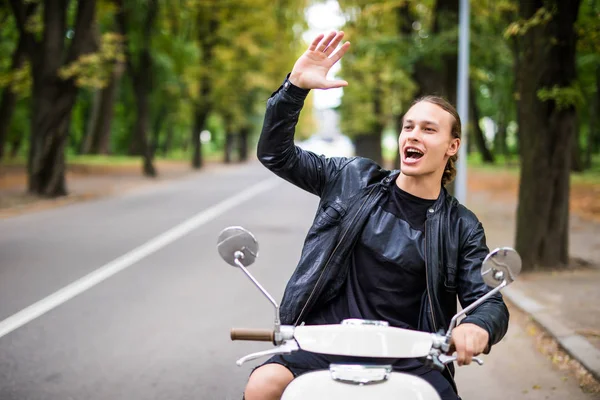 Kask içinde neşeli genç adam şehir sokak scooter ve demek Merhaba yolculuk sırasında oturuyor.