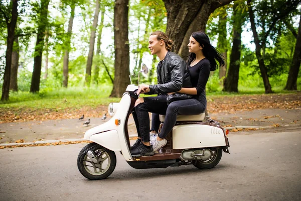 Belo jovem casal montando scooter juntos, mulher abraçando seu namorado. Vista lateral sobre a velocidade . — Fotografia de Stock