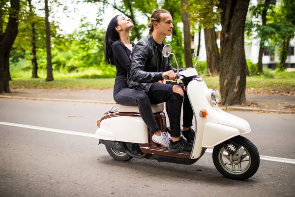 Belo jovem casal montando scooter juntos, mulher abraçando seu namorado. Vista lateral sobre a velocidade . — Fotografia de Stock