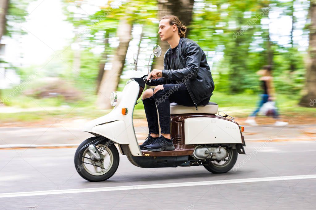 Side view of a handsome man riding a motorbike in the city street on speed