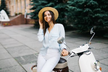 Yaşam tarzı görüntü gündelik kıyafeti scooter sokakta oturan genç moda kadın kadar kapatın. Giyiyor mavi tişört, beyaz pantolon, trendy güneş gözlüğü.