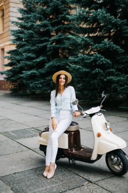 Yaşam tarzı görüntü gündelik kıyafeti scooter sokakta oturan genç moda kadın kadar kapatın. Giyiyor mavi tişört, beyaz pantolon, trendy güneş gözlüğü.