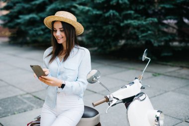 Onun motosiklet tarafından duran bir akıllı telefon kullanan genç kadın