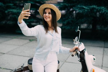 Bir vintage scooter ve yapmak telefon bir selfie üzerinde oturan genç kadın